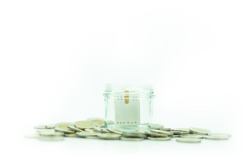 Mini wood house model cover by jar glass with many coins around on a white background.