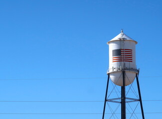 White water tank with American flag painted on the side. Blue sky. Americana.