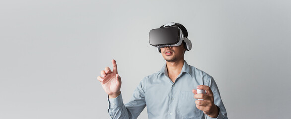 Excited young Asian wearing VR headset using with joystick on web banner grey background. © ME Image