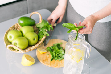 Woman in sportswear makes detox drink with lemon mint in kitchen at home. Rejuvenating invigorating water lemon,