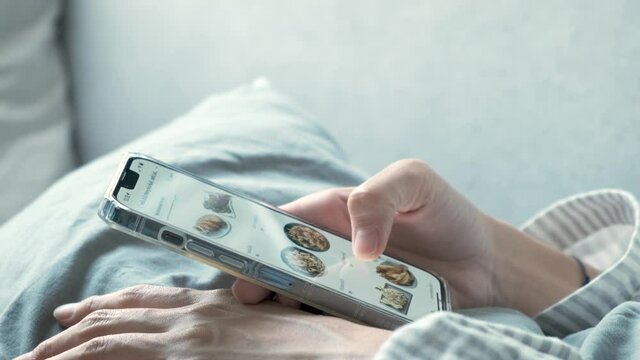 woman's hand sliding the phone screen in application Ordering food and beverages online home delivery In the morning wearing pajamas during the corona virus quarantine.