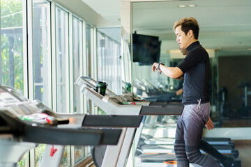 Active Asian sportsman making a cardio exercise by running on the treadmill machine in a fitness gym.