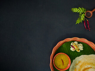traditional south indian food masala dosa, sambar and coconut chutney served on clay plate and banana leaf. studio shot.