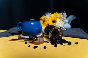 Blue mug of coffee on yellow background and coffee beans