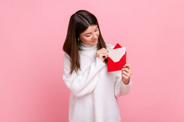 Portrait of happy woman holding red romantic envelope and looking at letter with smile and...