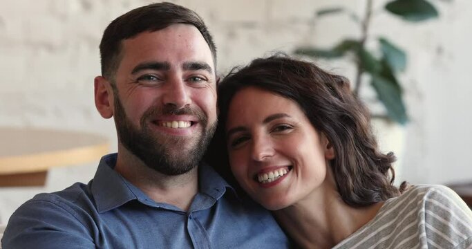 Happy couple in love relax on sofa smile looking at camera. Beautiful spouses sit indoor staring aside daydreaming, enjoy free time on weekend at own house. Homeowners family close up portrait concept