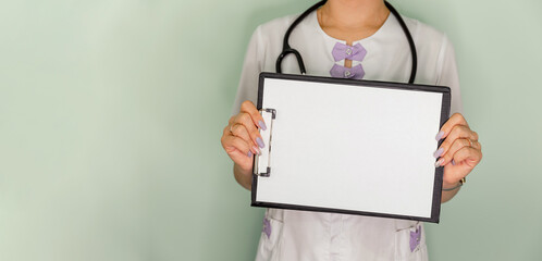 Female holding a blank sheet of paper with space for text. Medical clipboard. Doctor holding blank white banner in his hand. Young female doctor with paper holder. A doctor in a white uniform