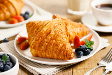breakfast with croissants and fresh berries on wooden table.