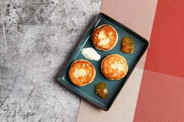 Cottage cheese pancakes with apricot jam on a rectangular   plate on a dark background. Top view, flat lay