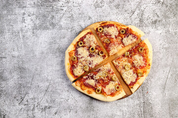 Sliced homemade pizza with pepperoni and olives on a dark grey background. Top view, flat lay