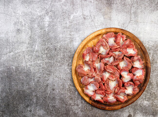 Raw chicken gizzards on a round wooden cutting board on a dark grey background. Top view, flat lay