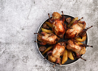 Roasted quails on a round plate on a dark background. Top view, flat lay