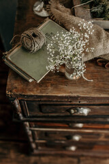 Vintage composition of wildflowers, rope coil, books and chest of drawer