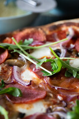 Homemade pizza with tomato sauce, sausage and arugula salad with onions on a wooden board with a knife. Front view.
