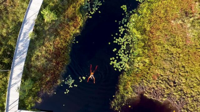 A rising aerial of a girl swimming in a bog lake in Soomaa, Estonia