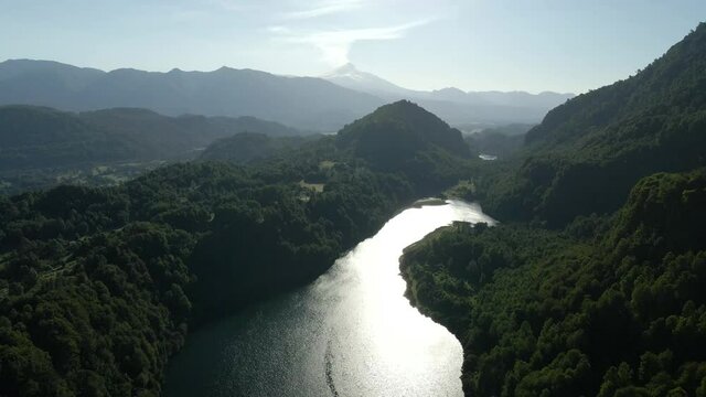 Drone shot of el leon lagoon surrounded by mountains in the background of villarica volcano on sunny day - aerial