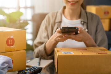 Startup small business, woman hand using smartphone with scan QR code on cardboard box delivery for products to send to customers.