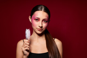 fashionable woman pink face makeup posing attractive look with a comb pink background unaltered