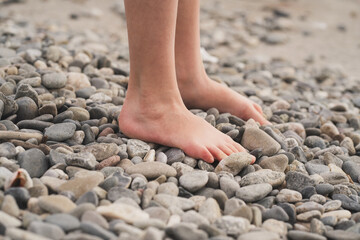 Prevention of flat feet in children. The child walks on the stones with his bare feet. Treatment of valgus foot in children and adults. Close-up of the child's foot on the rocks