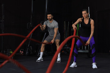 Obraz na płótnie Canvas Athletic young couple with battle rope doing exercise in functional training fitness gym.