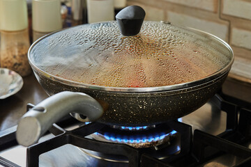 Frying pan on gas stove with the texture of drops on a glass lid with selective focus, background