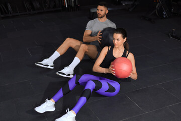 Beautiful young sports couple is working out with medicine ball in gym.