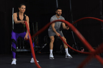 Athletic young couple with battle rope doing exercise in functional training fitness gym.