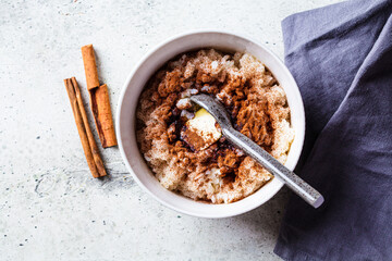 Scandinavian rice porridge with cinnamon and butter in white bowl on gray background. Norwegian cuisine concept.