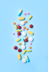 Vertical image of assorted multicolored medicine pills, capsules and tablets on pastel blue background. Immune system vitamins and supplemets. Various dietary bio supplements