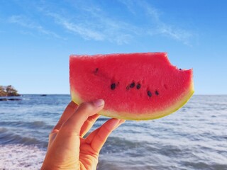 Holding a slice of bitten watermelon with blue sky and sea background