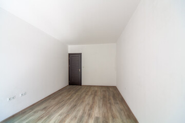 Fototapeta na wymiar Closed wooden door in empty bright room. New home interior. Wooden floor. White walls