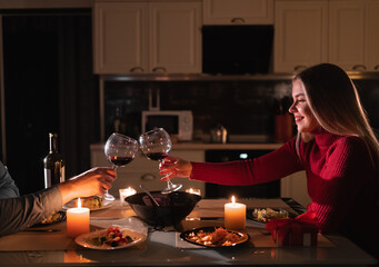 Couple clinking glasses at Valentine's day dinner. Romantic for two, date in the evening at home, toasting to valentine's day, glasses of red wine