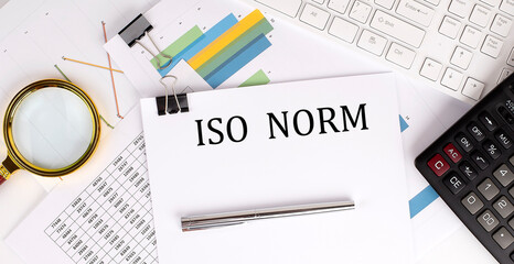 ISO NORM text on the white paper on the light background with charts paper ,keyboard and calculator - obrazy, fototapety, plakaty