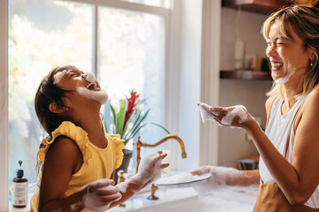 Playful mother and daughter having fun with soap foam