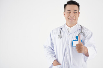 Fototapeta premium Portrait of smiling general practitioner showing thumbs-up, isolated on white