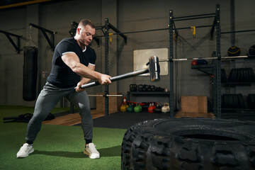 Sportsperson slamming training tool into tire during workout
