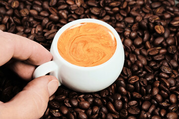 Man holds a cup of espresso coffee, top view, close-up on the cup. White cup with espresso coffee and coffee beans on background. Italian coffee for breakfast