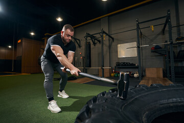 Concentrated sportsman performing tire slam exercise at gym