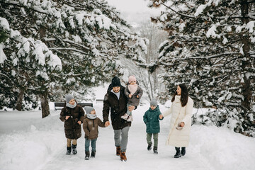 Big happy family spending time outdoors on snowy winter day, walking in a park.