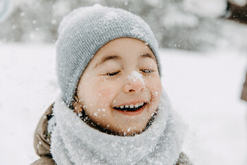 Closeup portrait of a little boy with snow on his nose, laughing, with eyes closed, on cold winter...