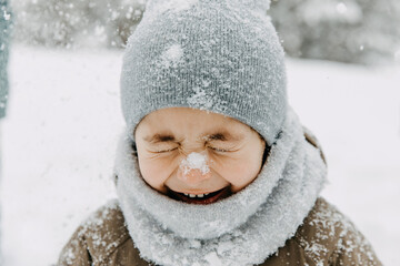Closeup portrait of a little boy with snow on his nose, laughing, with eyes closed, on cold winter day.
