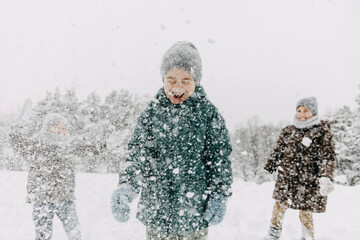 Boys playing outdoors on a snowy winter day in a forest, laughing, having fun, throwing snow at each other.