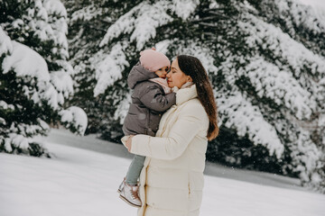 Mother cuddling with little daughter, outdoors on a snowy winter day.
