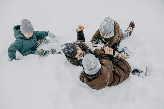 Father playing with children on snowy winter day, fighting on snow and laughing.
