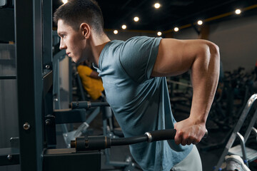 Concentrated sportsman doing strength-training exercise on fitness machine