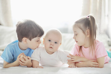 Children lie on the bed next to the newborn baby, little sister.