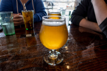 View of a frothy, ice cold farmhouse ale on a wooden table inside a restaurant