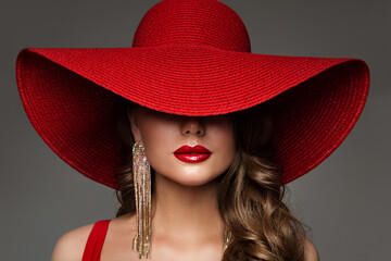 Fashion Woman in Hat with Red Lips Make up and Golden Earring. Beauty Model Face Hidden by Wide Broad Brim Hat. Elegant Lady Close up Portrait over Gray - obrazy, fototapety, plakaty