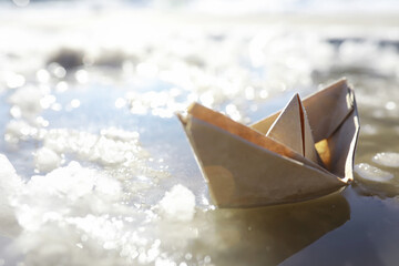 Paper boat in the water on the street. The concept of early spring. Melting snow and an origami boat on water waves.