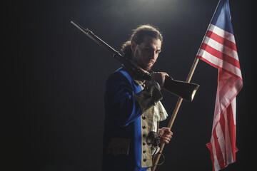 American revolution war soldier with flag of colonies and musket gun over dramatic smoke background. 4 July independence day of USA concept photo composition: soldier and flag.